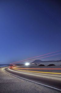 Light trails over road against clear blue sky at dusk