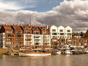 Sailboats moored on river by buildings against sky