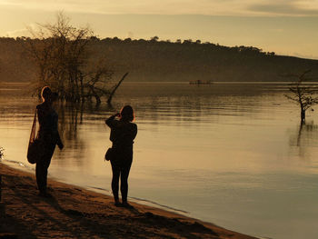Full length of women standing at lakeshore during sunset