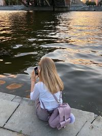 Woman photographing with mobile phone while sitting on lake