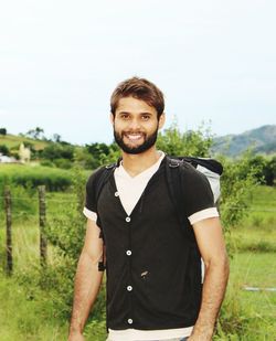 Portrait of smiling young man standing on grassy field against sky