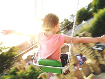Rear view of girl with arms outstretched sitting in chain swing ride