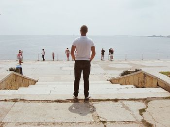 Rear view of man looking at sea while standing on promenade against sky