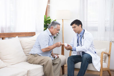 Doctor showing medicine to patient while sitting on sofa at hospital