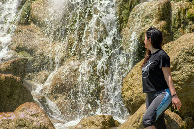 Rear view of woman standing on rock by waterfall