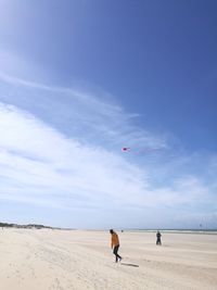 Full length of man flying kite at beach against blue sky