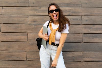 Portrait of young woman sticking out tongue against wall