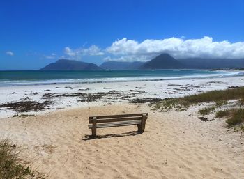 Empty bench at beach against sky