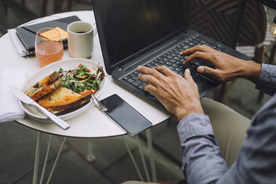 Hands of businessman using laptop by meal and smart phone on table