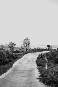 Dirt road amidst field against clear sky