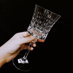Close-up of hand holding wineglass against black background