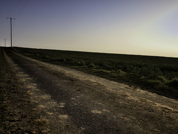 Dirt road amidst field against clear sky