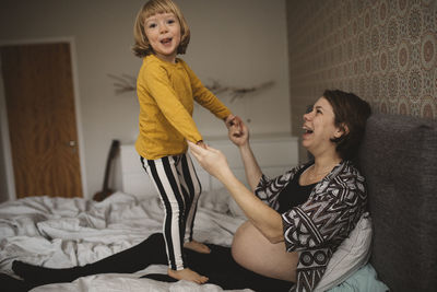 Girl holding hands with pregnant mother on bed