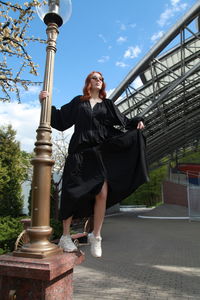 Full length of woman in oversized black dress walking to nowhere against built structure outdoors