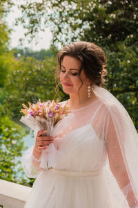 Beautiful smiling bride in traditional white wedding dress holding bouquet of dry homemade flowers. 