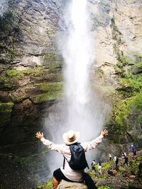 Rear view of man with arms outstretched looking at waterfall
