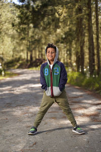 Smiling boy looking away while standing on footpath against trees