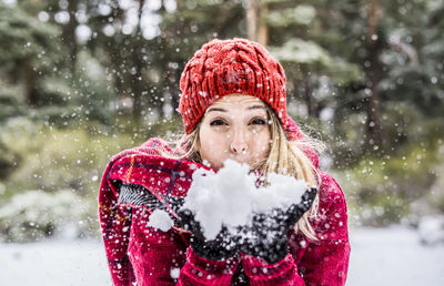Portrait of woman blowing snow while standing outdoors during winter