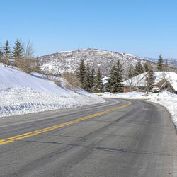 Road by snowcapped mountains against clear sky