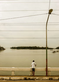 Rear view of man standing by railing against sky