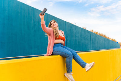 Young woman taking selfie against wall