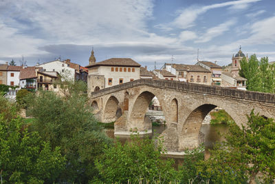 Arch bridge by buildings against sky in city