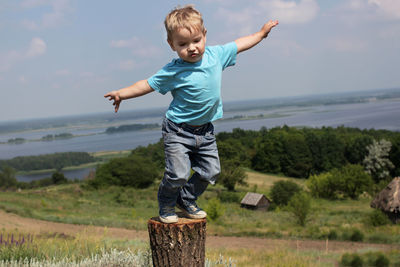 Cute small boy standing on hill with spreading hands over beautiful landscape, ready to jump