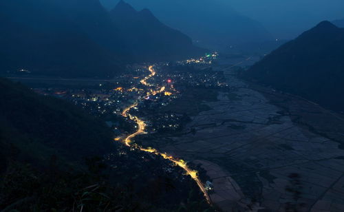 Aerial view of illuminated town amidst mountains at night