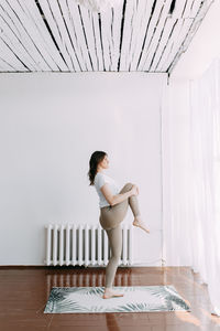 Side view of young woman standing on table against wall