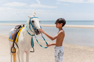 Young rider with horse standing on the beach.