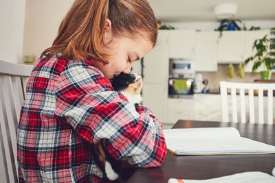 Rear view of girl with cat sitting on chair at home