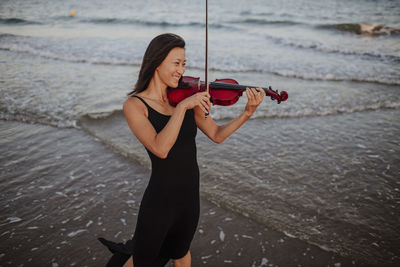 Happy woman playing violin in sea at beach