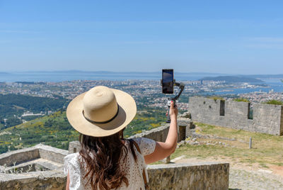 Young woman in white dress standing at klis fortress taking photos of city of split in croatia