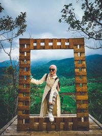 Young woman standing by tree against sky