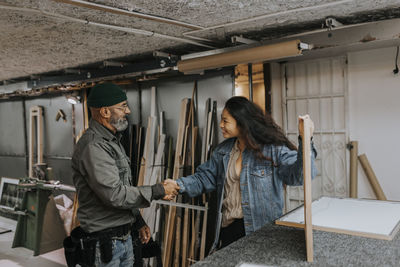 Smiling young woman shaking hands with craftsman in workshop