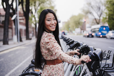 Beautiful woman holding electric bicycle at parking station in city