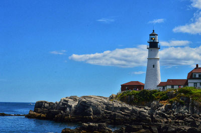 Lighthouse amidst buildings and sea against sky