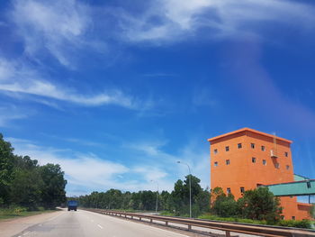 Road by buildings against blue sky