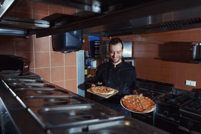 Smiling male chef looking at camera and showing a pizzas