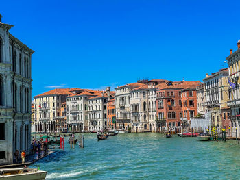 Buildings by river against clear blue sky