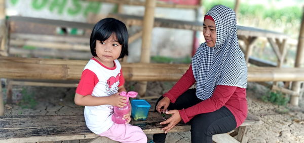 Mother wearing hijab sitting with daughter on bench
