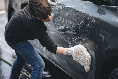 Side view of boy washing car on driveway