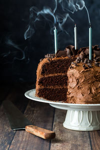 A triple layered chocolate cake with candles that have just been blown out.