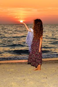 Rear view of woman standing on beach during sunset