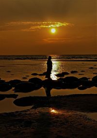 Silhouette man on beach against sky during sunset