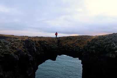 Man on a natural rock bridge between ocean and sky in arnarstapi
