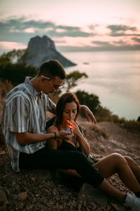 Young woman sitting on beach against sky during sunset