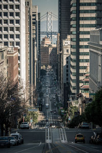 Road amidst buildings in city against san franciscooakland bay bridge