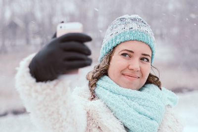 Smiling young woman taking selfie while standing at park during winter