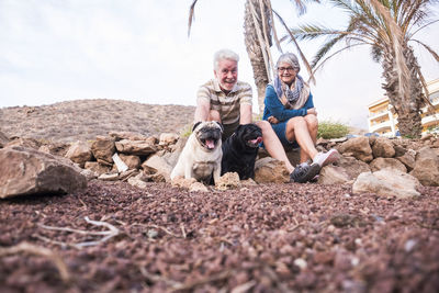 Senior couple with dogs sitting on rocks at field